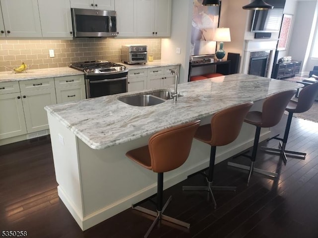 kitchen featuring a sink, stainless steel appliances, a kitchen breakfast bar, dark wood finished floors, and light stone countertops