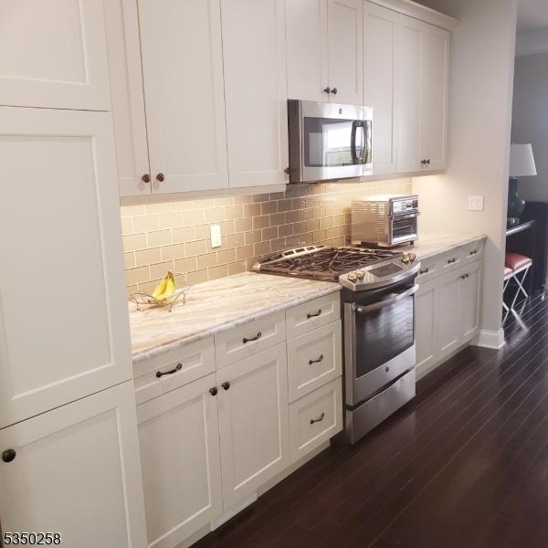kitchen featuring dark wood finished floors, white cabinetry, decorative backsplash, and appliances with stainless steel finishes