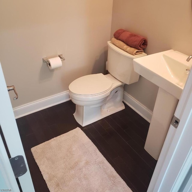 half bathroom with toilet, baseboards, and wood finished floors