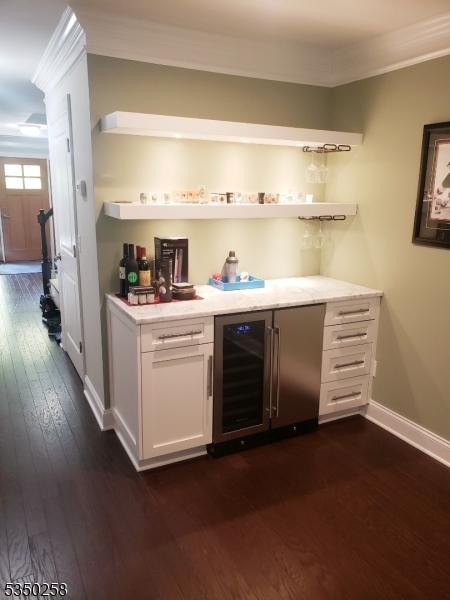 bar with a bar, dark wood finished floors, baseboards, ornamental molding, and wine cooler