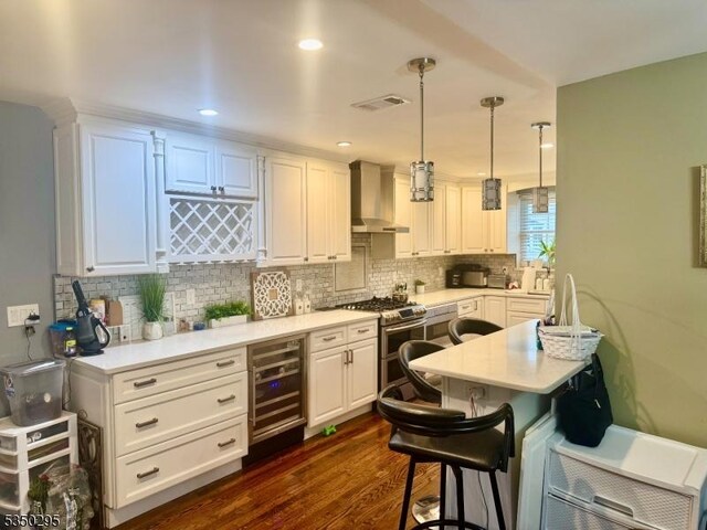 kitchen with double oven range, wall chimney exhaust hood, beverage cooler, light countertops, and white cabinets
