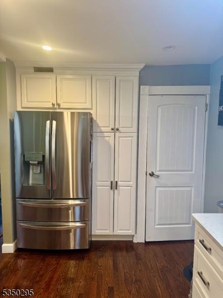 kitchen with stainless steel fridge, dark wood finished floors, white cabinets, and light stone countertops