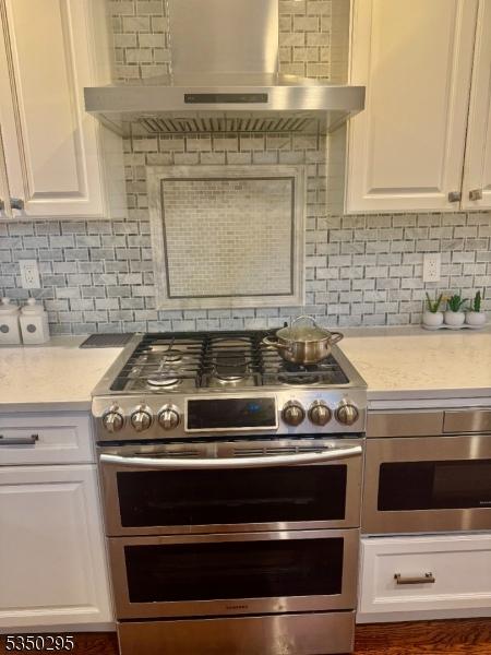 kitchen with range with two ovens, range hood, white cabinets, and light countertops