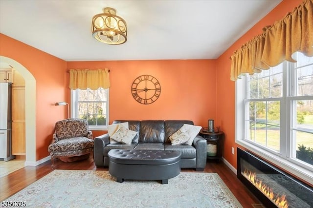 living room featuring arched walkways, wood finished floors, and a healthy amount of sunlight