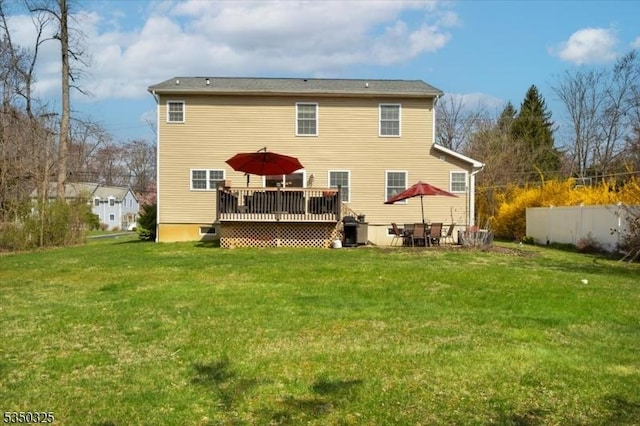 back of property featuring fence, a wooden deck, and a lawn