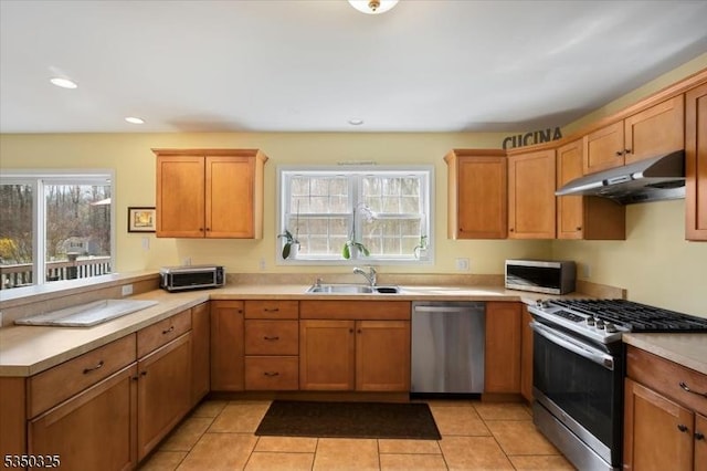 kitchen featuring a wealth of natural light, a peninsula, under cabinet range hood, a sink, and stainless steel appliances