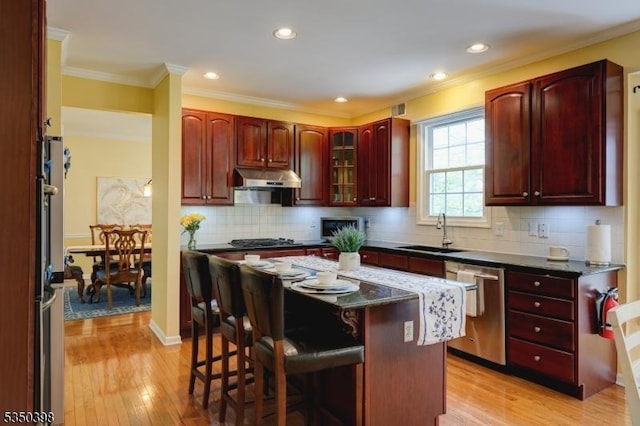 kitchen featuring stainless steel dishwasher, a sink, reddish brown cabinets, a breakfast bar, and under cabinet range hood