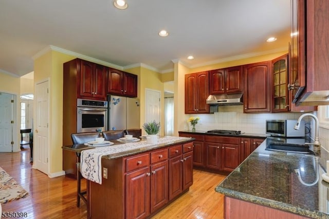 kitchen featuring stainless steel oven, a sink, reddish brown cabinets, dark stone counters, and ornamental molding