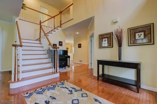 staircase with hardwood / wood-style flooring, baseboards, a towering ceiling, and crown molding