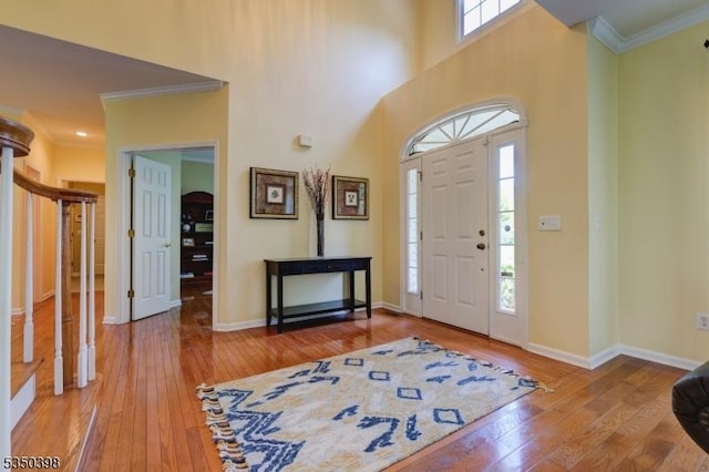 foyer featuring wood-type flooring, ornamental molding, baseboards, stairs, and a towering ceiling