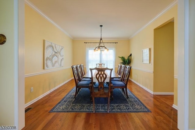 dining room with wood finished floors, baseboards, ornamental molding, and a chandelier