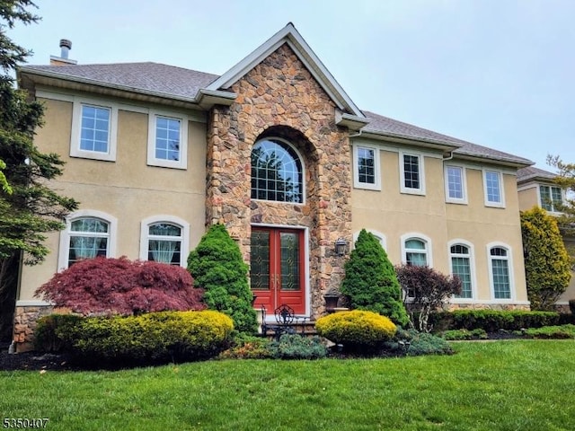 view of front of house featuring stone siding, stucco siding, a chimney, and a front yard