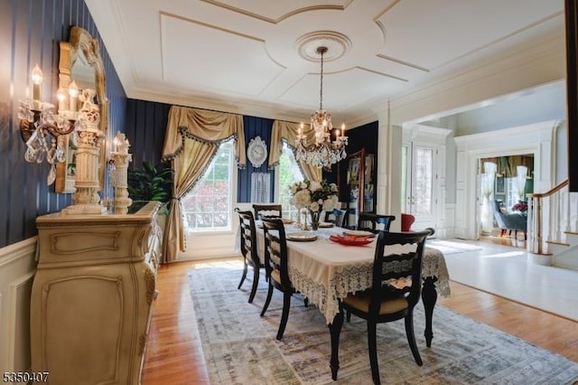 dining area featuring light wood-style flooring, a notable chandelier, crown molding, a decorative wall, and stairs