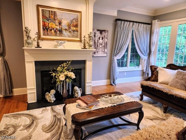 living room with ornamental molding, baseboards, a glass covered fireplace, and wood finished floors