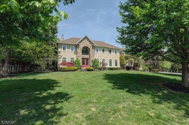 colonial home featuring stone siding, a front lawn, and a chimney