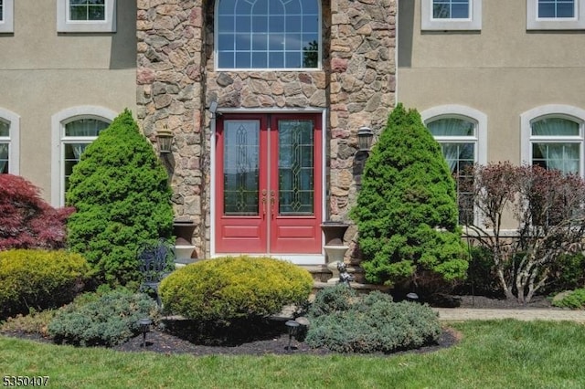 view of exterior entry featuring stone siding, stucco siding, and french doors