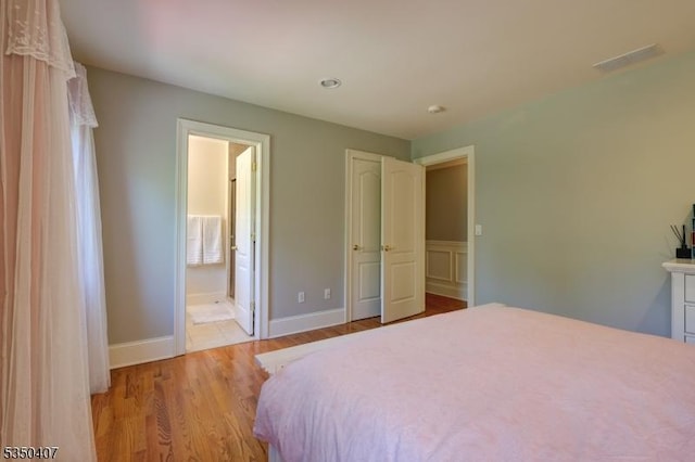 bedroom featuring ensuite bath, visible vents, light wood-style flooring, and baseboards