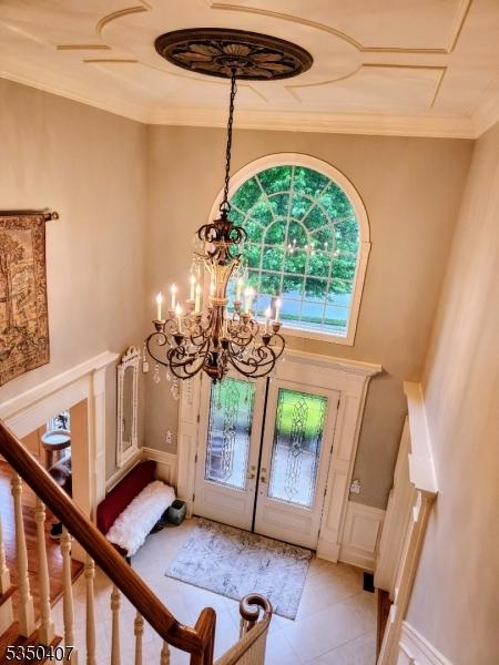 foyer with a decorative wall, a wainscoted wall, french doors, ornamental molding, and an inviting chandelier