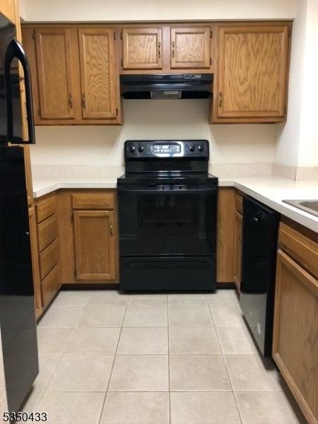 kitchen with brown cabinets, range hood, light countertops, and black appliances