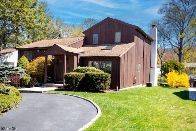 view of front facade with a shingled roof, a chimney, and a front lawn