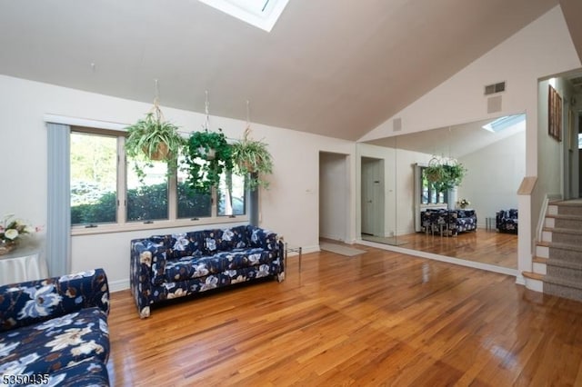 living room with visible vents, a skylight, wood finished floors, high vaulted ceiling, and stairs