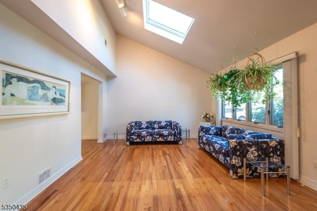 interior space featuring visible vents, wood finished floors, baseboards, high vaulted ceiling, and a skylight