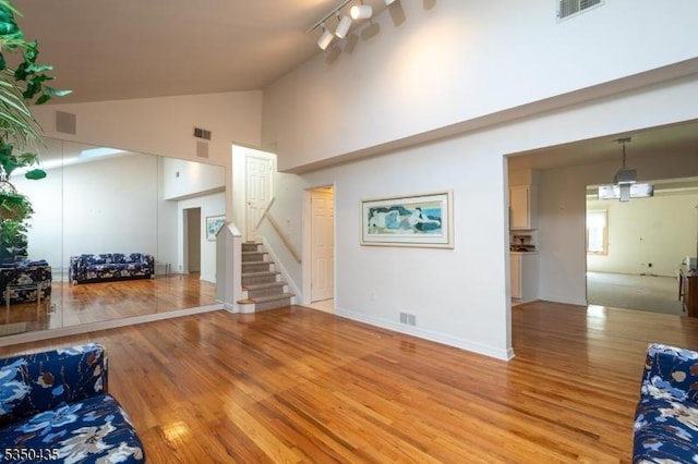 living area featuring stairs, high vaulted ceiling, visible vents, and light wood-style flooring