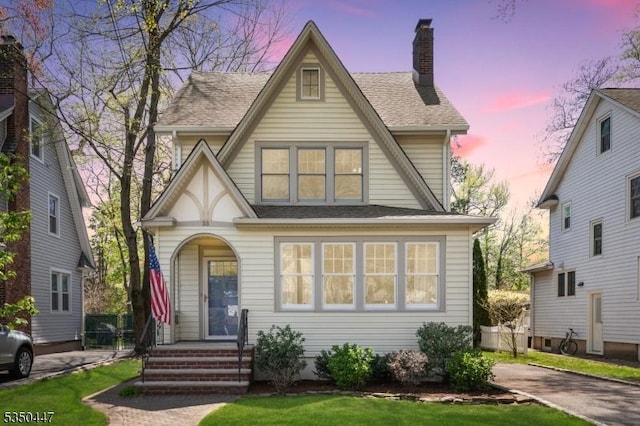 english style home with a shingled roof, a chimney, and a front yard