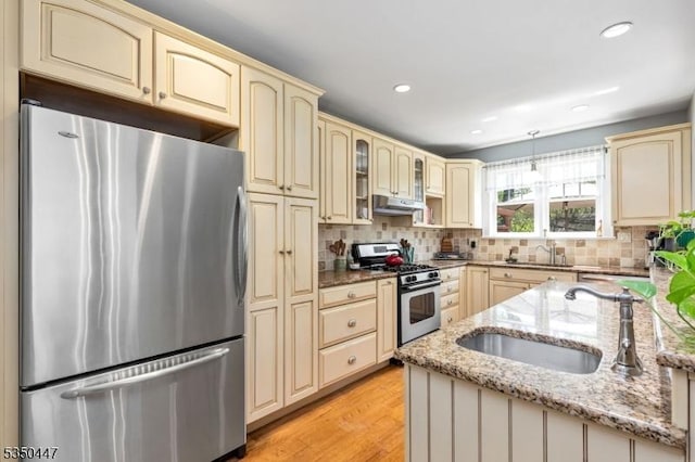 kitchen with a sink, under cabinet range hood, stainless steel appliances, and cream cabinetry