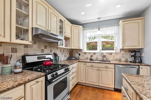 kitchen with appliances with stainless steel finishes, cream cabinets, a sink, light wood finished floors, and under cabinet range hood