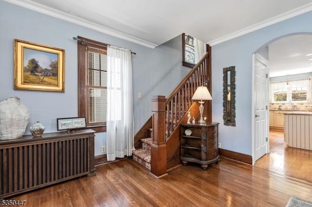 interior space featuring crown molding, arched walkways, baseboards, and wood finished floors