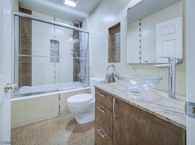 bathroom with toilet, tile walls, tile patterned flooring, vanity, and tiled shower / bath