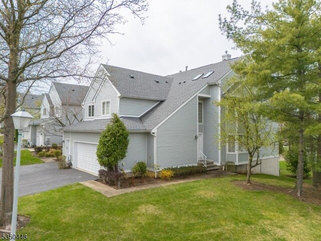 view of property exterior featuring entry steps, an attached garage, a shingled roof, a yard, and aphalt driveway