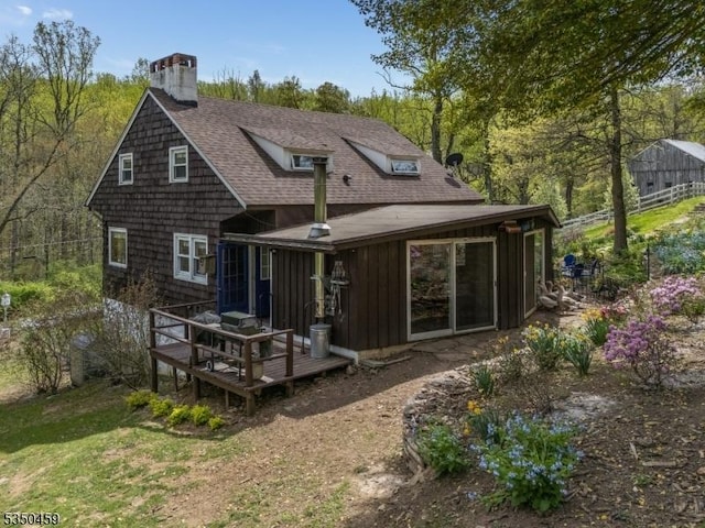 back of house with a deck, a chimney, a shingled roof, board and batten siding, and a yard