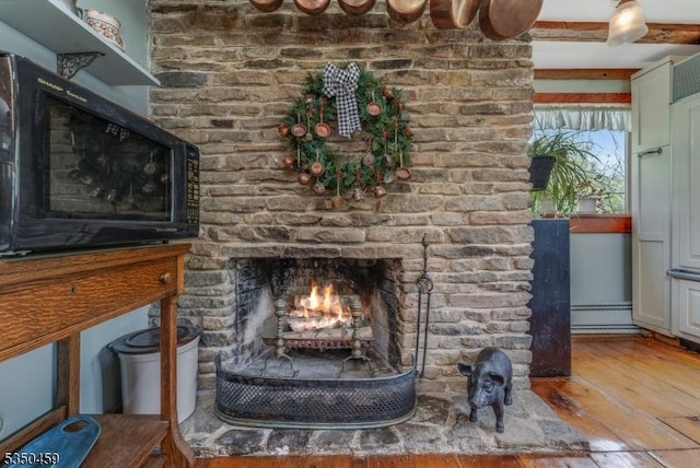 details with wood finished floors, a baseboard heating unit, black microwave, and a fireplace