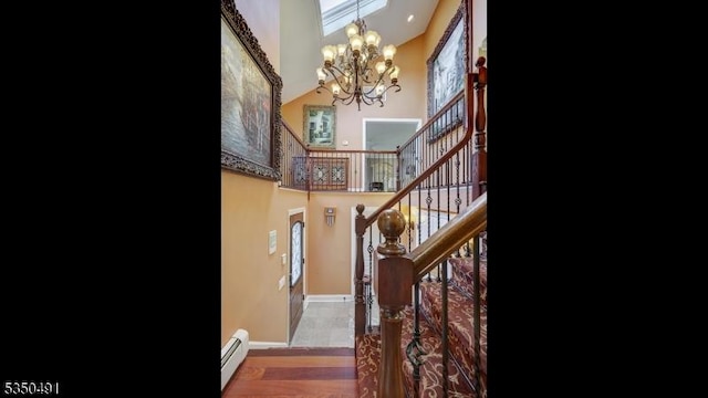 staircase with a baseboard heating unit, baseboards, a high ceiling, and an inviting chandelier