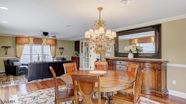 dining space featuring visible vents, ornamental molding, baseboards, light wood-style flooring, and ceiling fan with notable chandelier