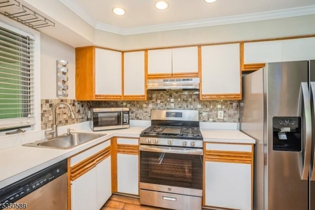 kitchen featuring stainless steel appliances, under cabinet range hood, light countertops, a sink, and crown molding