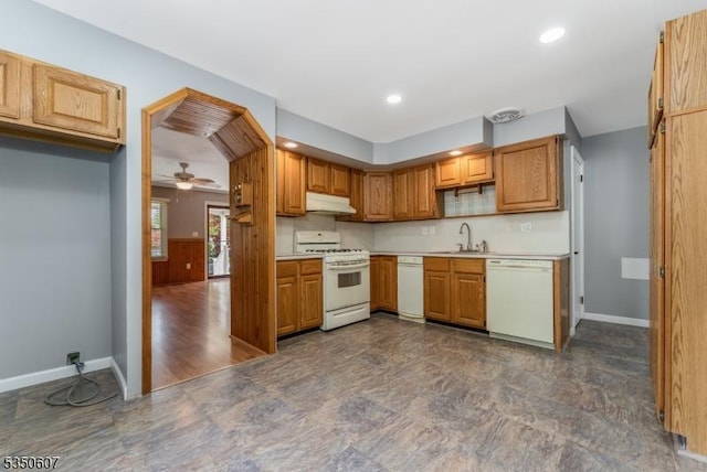 kitchen featuring a sink, white appliances, light countertops, baseboards, and under cabinet range hood