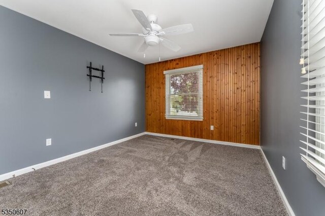 carpeted empty room featuring baseboards, a ceiling fan, and wood walls