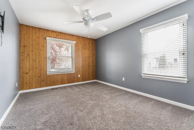 spare room featuring baseboards, wood walls, and carpet