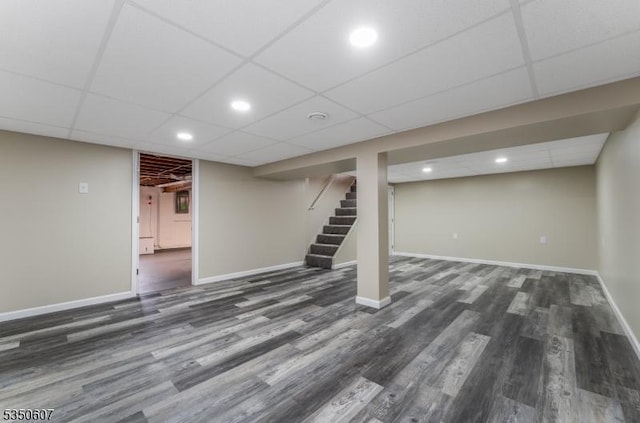 finished basement with a paneled ceiling, stairs, recessed lighting, baseboards, and dark wood-style floors
