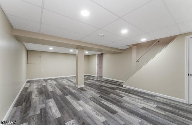 finished below grade area with stairs, wood finished floors, baseboards, recessed lighting, and a paneled ceiling