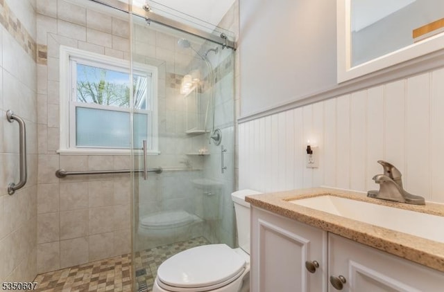 bathroom with vanity, a wainscoted wall, toilet, and a shower stall