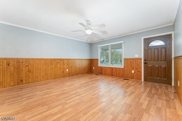 foyer featuring ceiling fan, light wood-style floors, wood walls, a wainscoted wall, and ornamental molding
