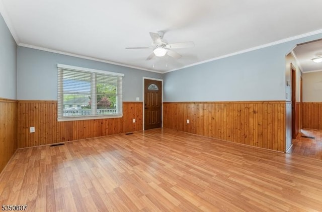 empty room with wainscoting, light wood finished floors, and ceiling fan