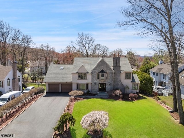 french provincial home with a front lawn, driveway, stone siding, a chimney, and stucco siding