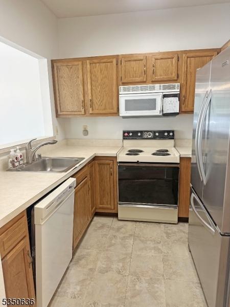 kitchen featuring white appliances, brown cabinetry, a sink, and light countertops