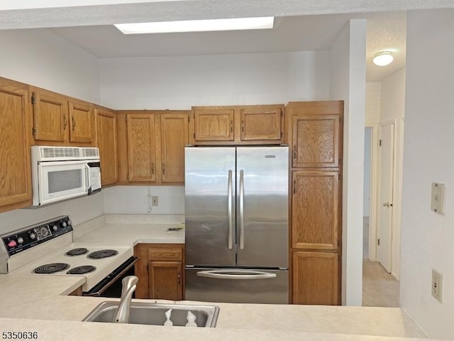 kitchen with a sink, brown cabinets, white appliances, and light countertops
