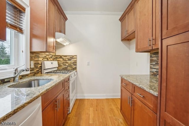 kitchen featuring brown cabinets, under cabinet range hood, a sink, and white appliances